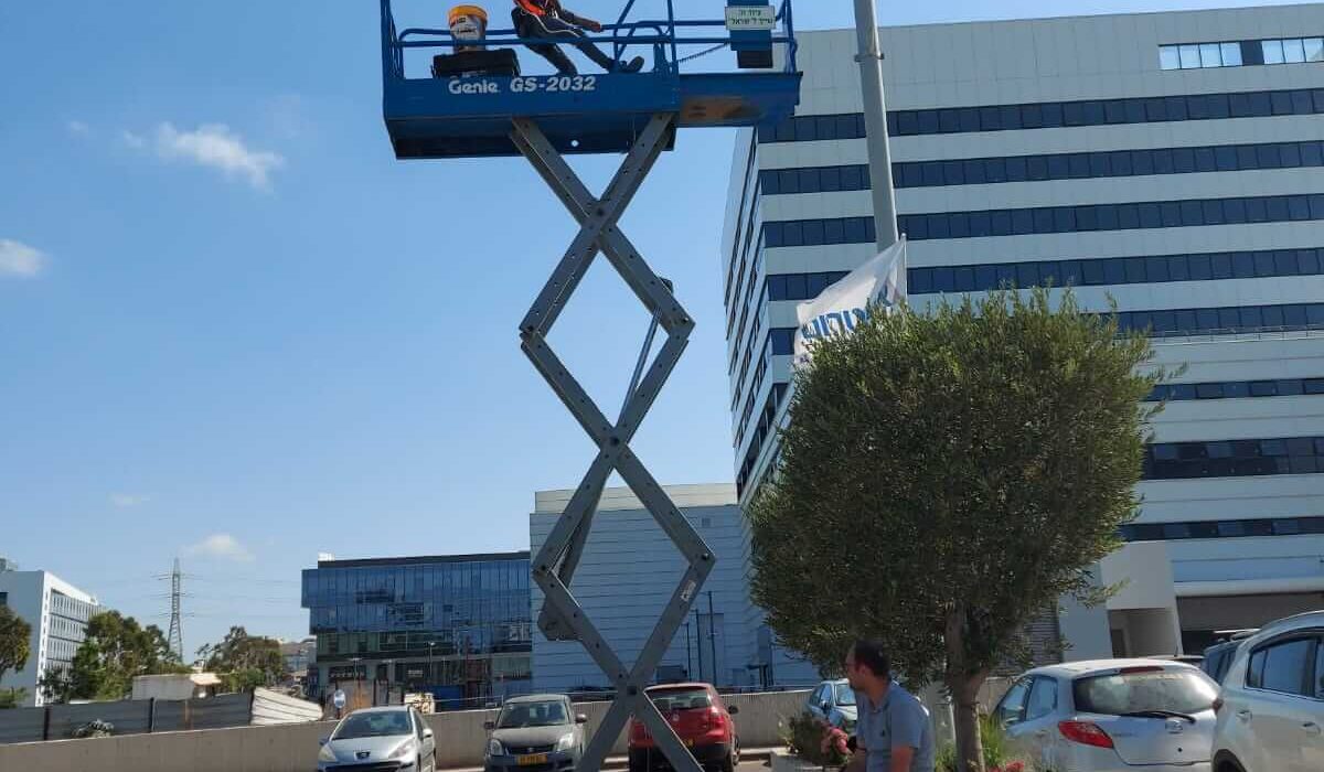 • החלפת מנורות לעמודים בחניון במסגרת עבודה בגובה עם במת הרמה, מבוצע על ידי חשמלאי מקצועי ומורשה לעבודות בגובה.